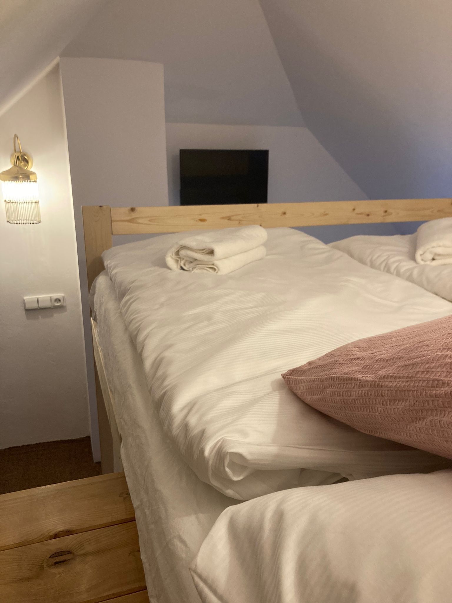 A bedroom with a wooden headboard, a flat-screen TV mounted on the wall, and a bedside lamp.
