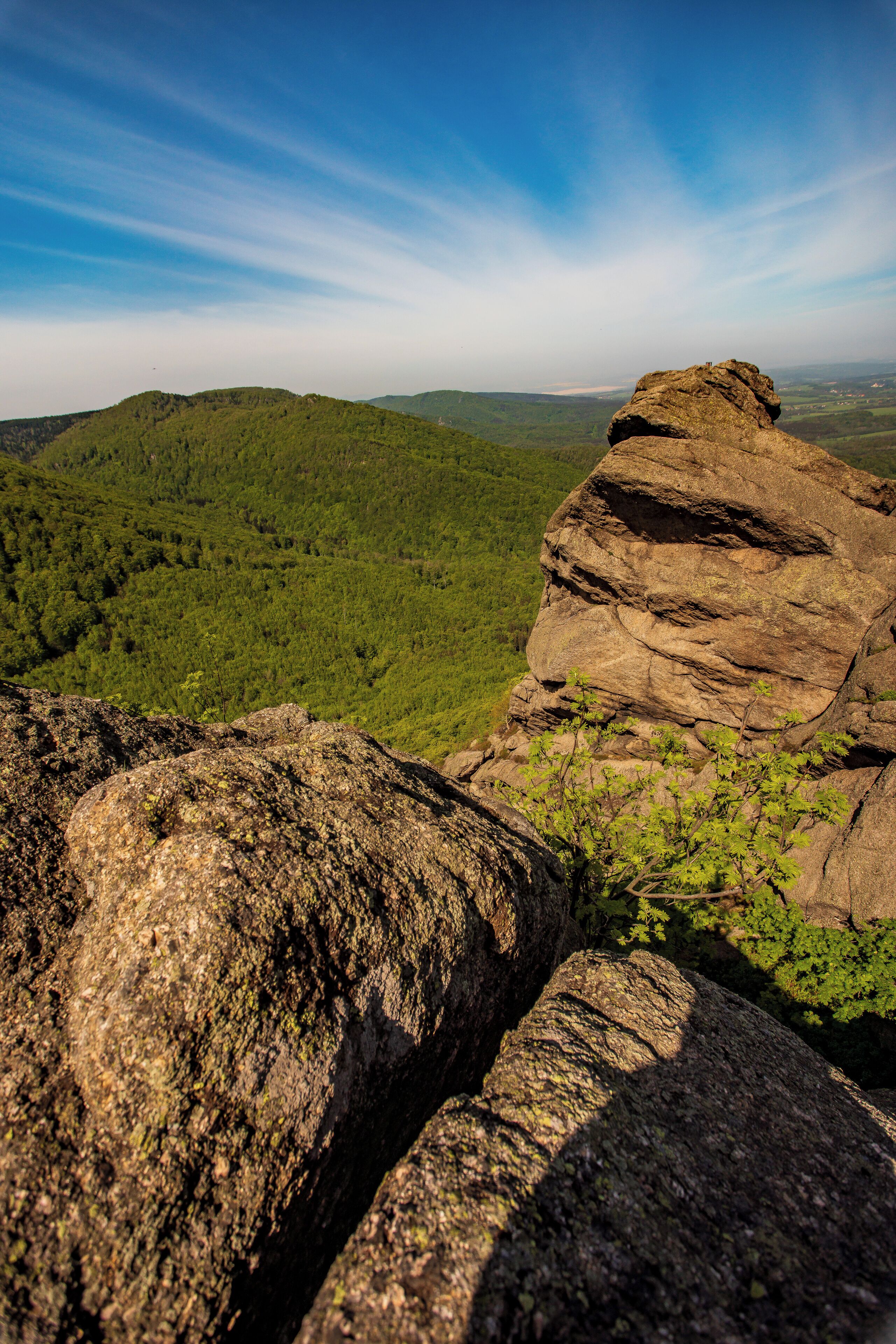 A rocky landscape with a prominent rock formation and a view of a forested valley.