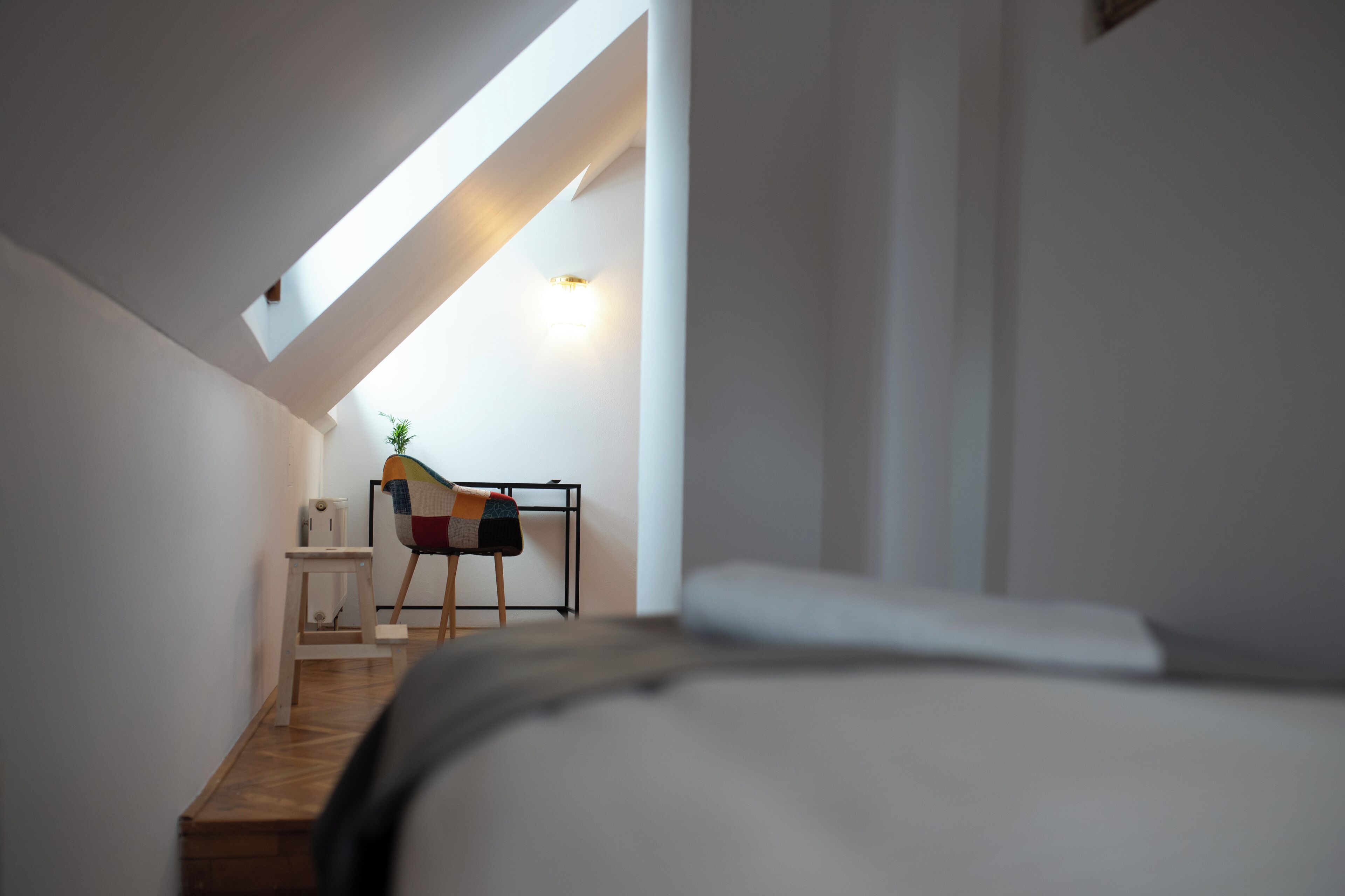 Un dormitorio moderno con techo inclinado, una cama, una mesita y una silla.