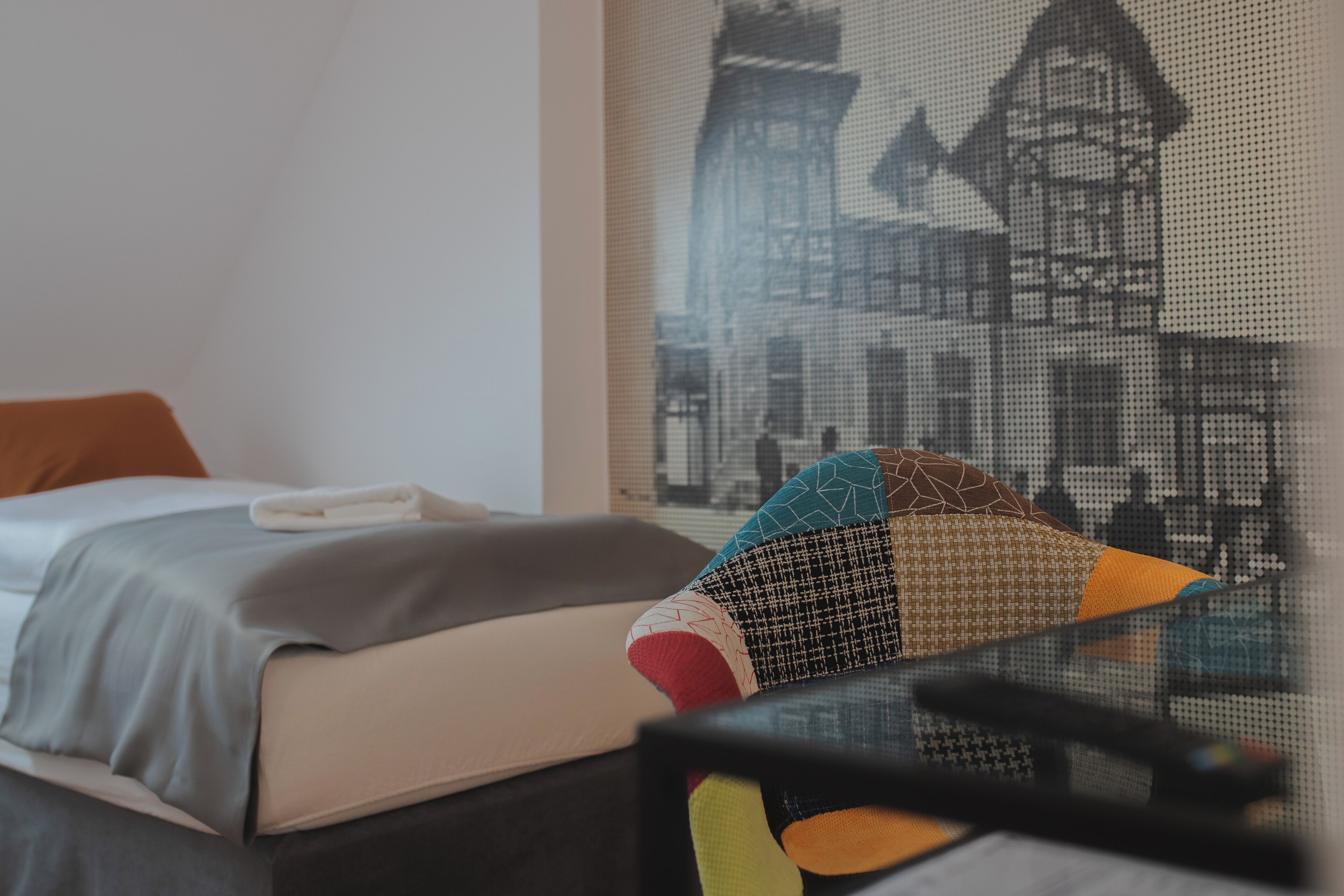 A hotel room with a bed, a window with a view of a building, and a wall with a patterned design.