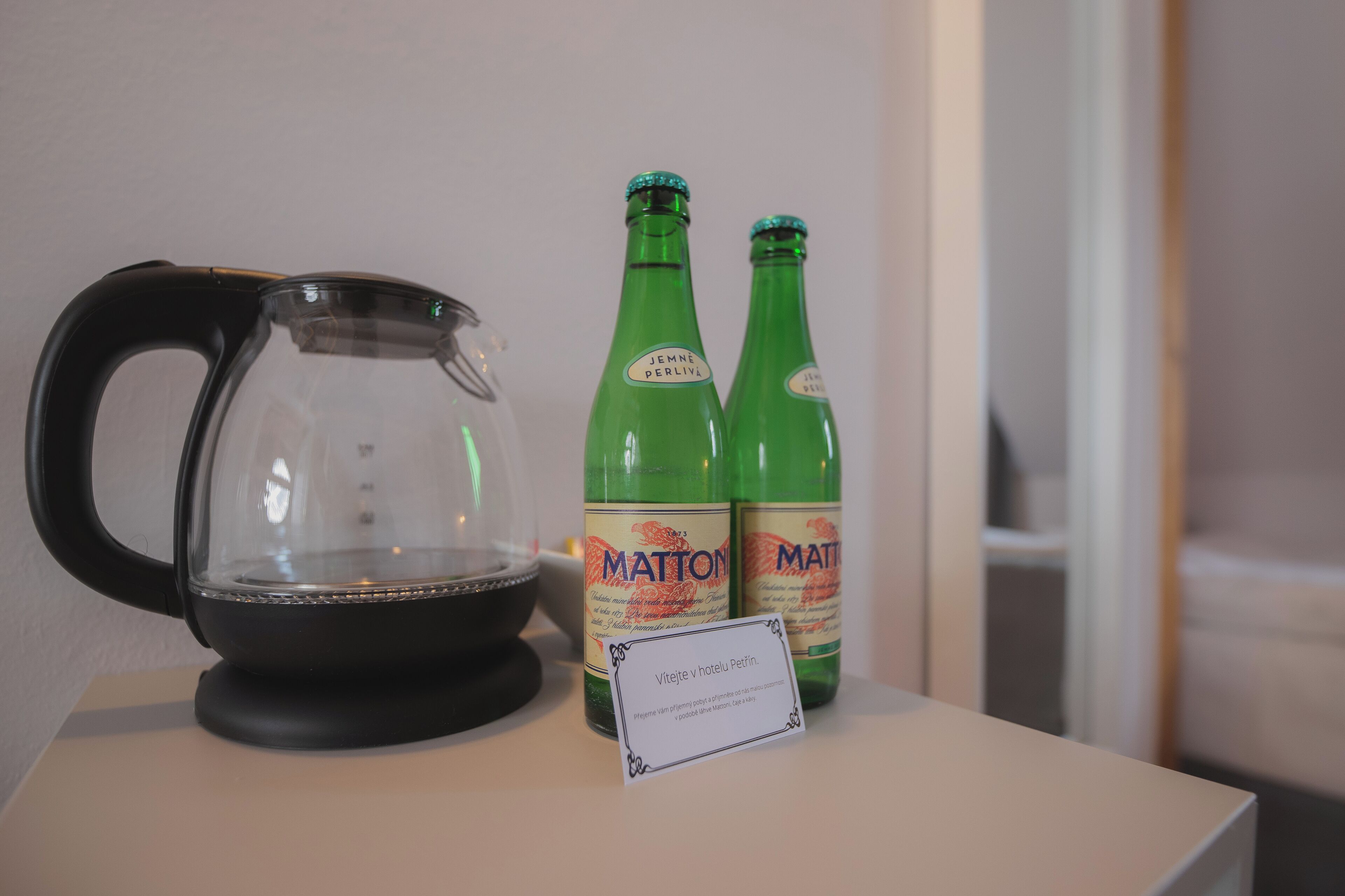 Eine transparente Kaffeekanne, zwei grüne Flaschen mit dem Aufdruck 'MATTON' und ein Schild mit Schrift in einer Fremdsprache.