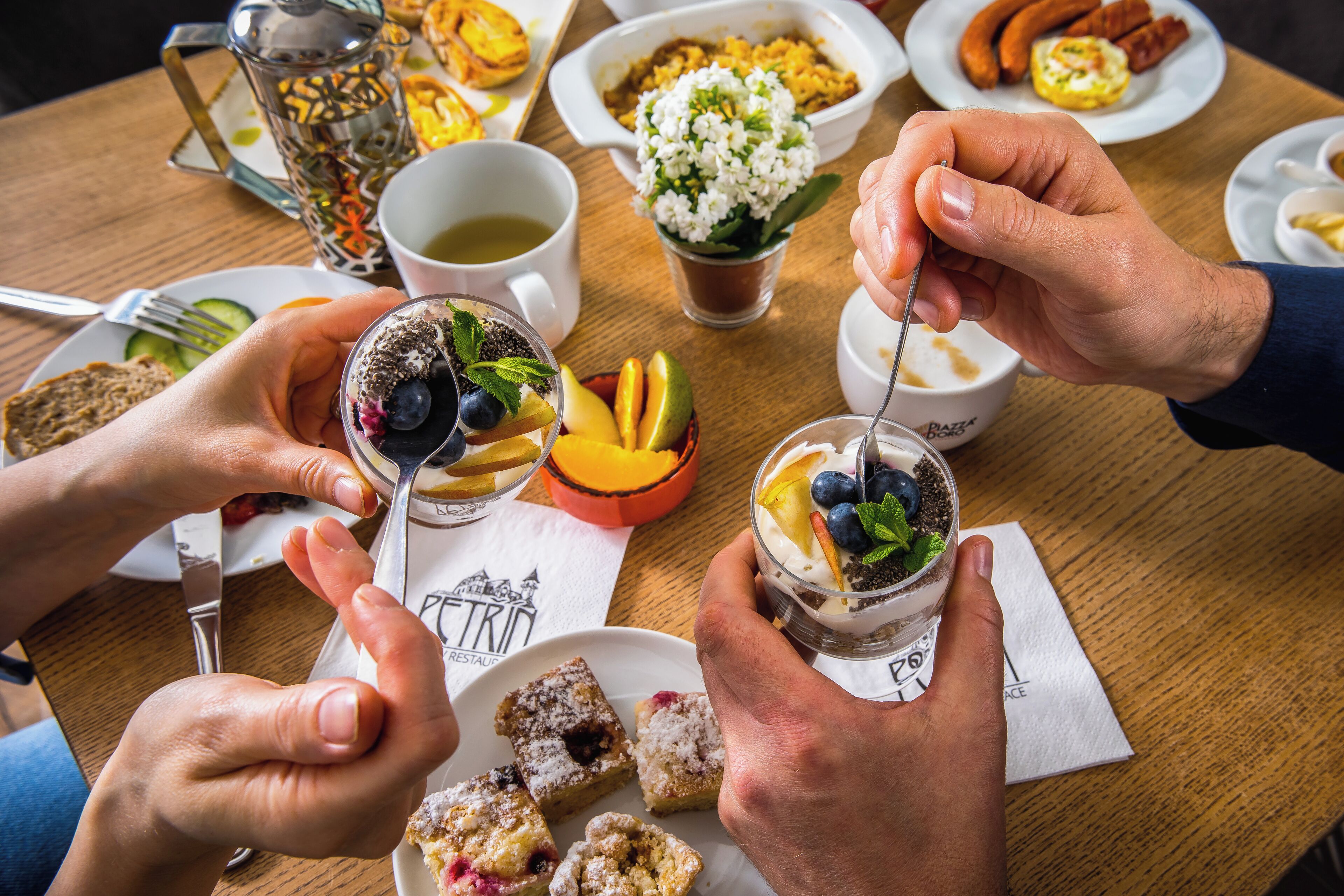 Una mesa de comedor con varios platos, incluyendo un plato de pasteles, un vaso de ensalada de frutas y una taza de café.
