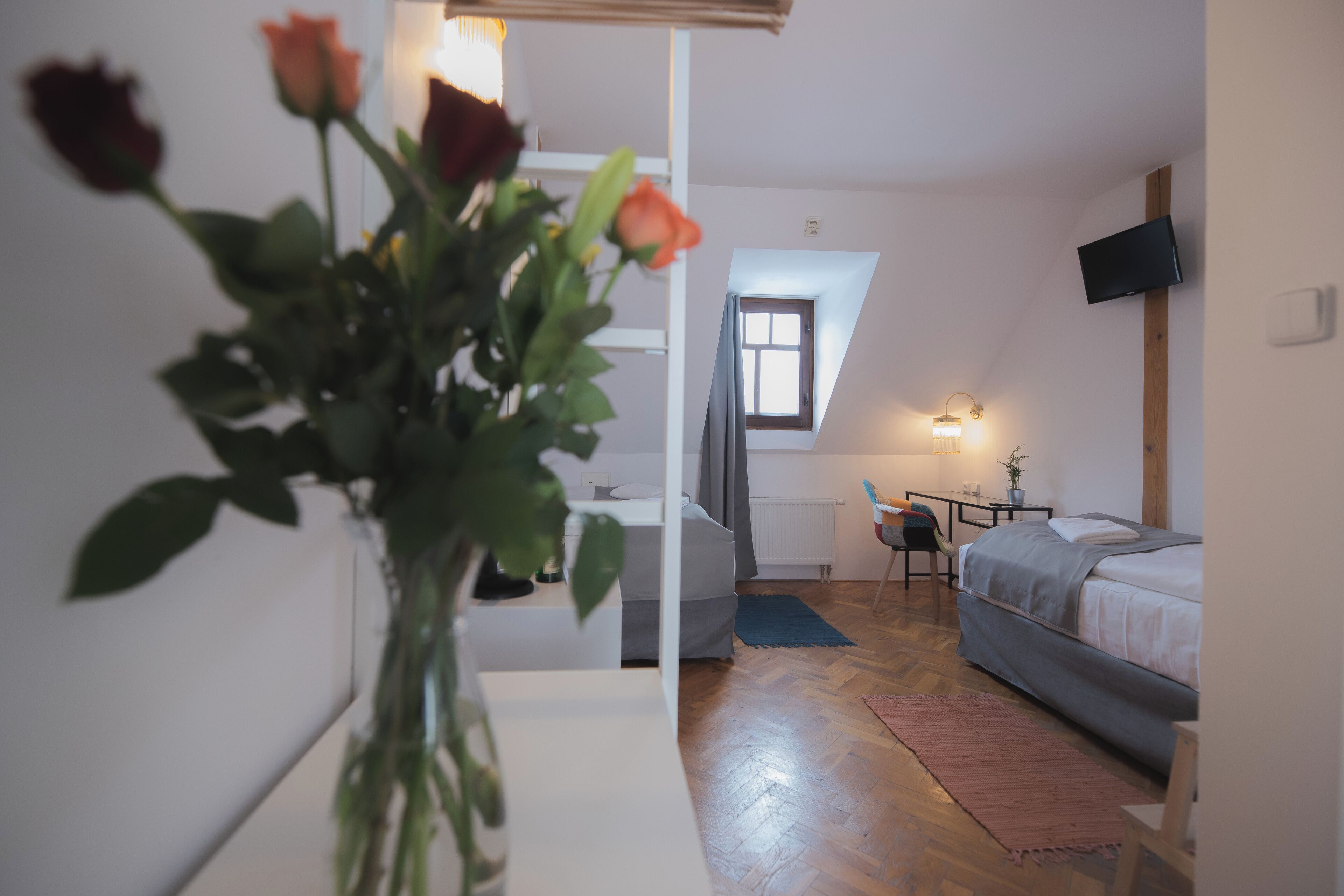 A bedroom with a bed, a desk, and a chair. There is a window with curtains and a plant in the corner.