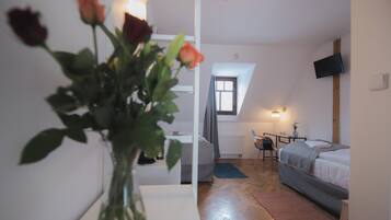 A bedroom with a bed, a desk, and a chair. There is a window with curtains and a plant in the corner.