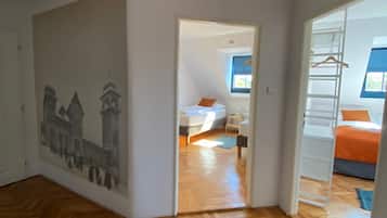 A spacious room with a wooden herringbone floor, a large window, and a bed with an orange blanket.