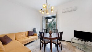 A modern living room with a sofa, dining table, chairs, a TV, and a ceiling light fixture. - 'Pegli Giardino District' Apartment with Sea View (Genova)