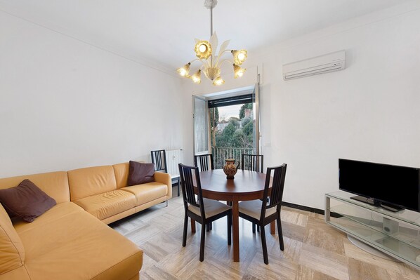 A modern living room with a sofa, dining table, chairs, a TV, and a ceiling light fixture.