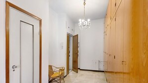 A hallway with a wooden wardrobe, a wicker chair, and a chandelier. - 'Pegli Giardino District' Apartment with Sea View (Genova)