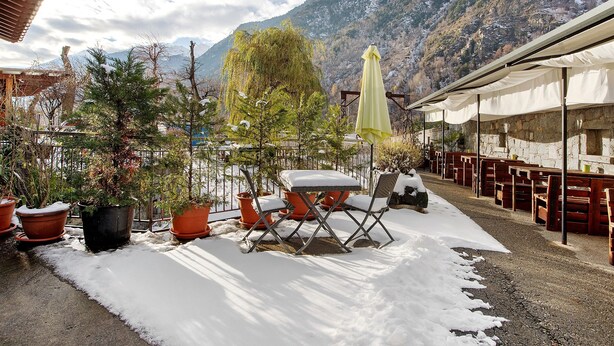 A patio area with potted plants, a folding chair, and a table with a snow-covered ground. - Room 'Camera Matrimoniale' with Mountain View, Shared Garden and Wi-Fi (Grosio)