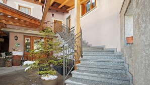 A stone staircase leading to a wooden upper level, a metal railing, and a small tree with snow on its branches. - Room 'Camera Matrimoniale' with Mountain View, Shared Garden and Wi-Fi (Grosio)