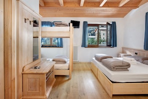 Ein Zimmer mit Etagenbetten, einem Holzschrank, einem Nachttisch, einem Fernseher und einem Fenster mit Vorhängen.