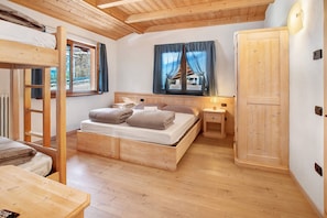 Ein Schlafzimmer mit Etagenbett aus Holz, einem Fenster, einem Nachttisch und einem Kleiderschrank.