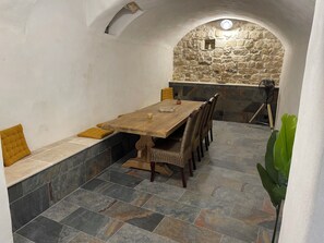 A dining area with a wooden table and chairs, a bench with cushions, stone walls, and a stone archway. - House in the Heart of the Village   (Cornillon)