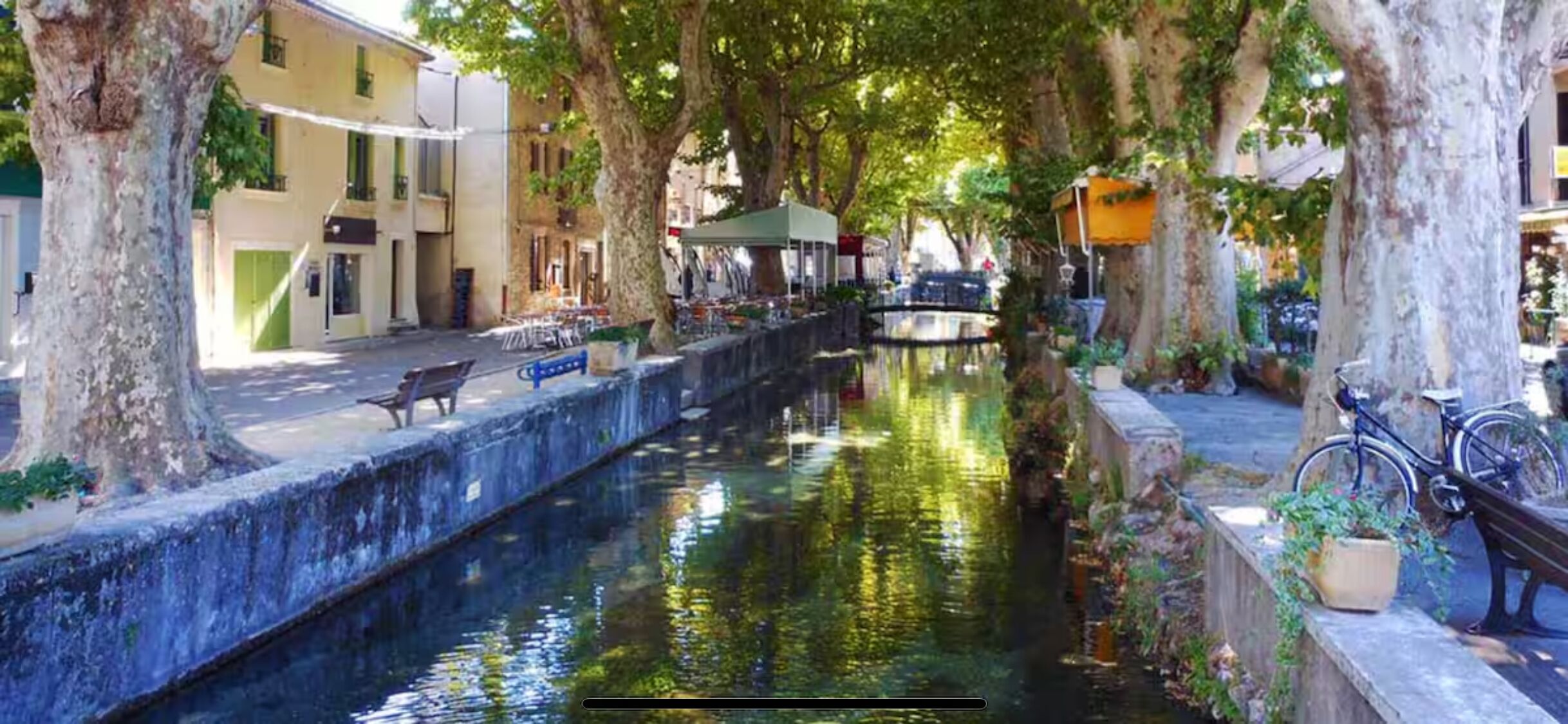 A narrow canal with a bench and a bicycle on the right side, surrounded by trees and buildings.