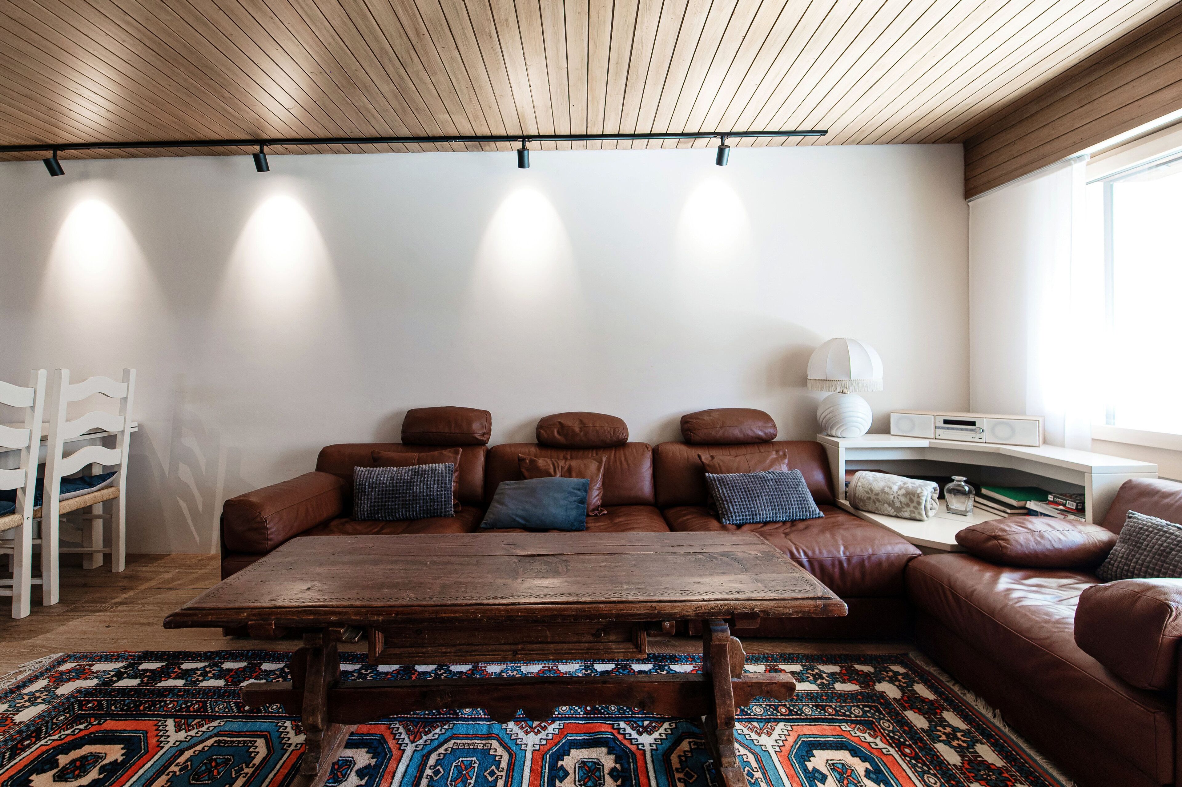 Ein Wohnzimmer mit Holzboden, einem braunen Ledersofa mit Kissen, einem Holztisch und einem gemusterten Teppich.
