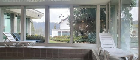 Un área de piscina interior moderna con dos sillones de descanso y un espacio de estar integrado.
