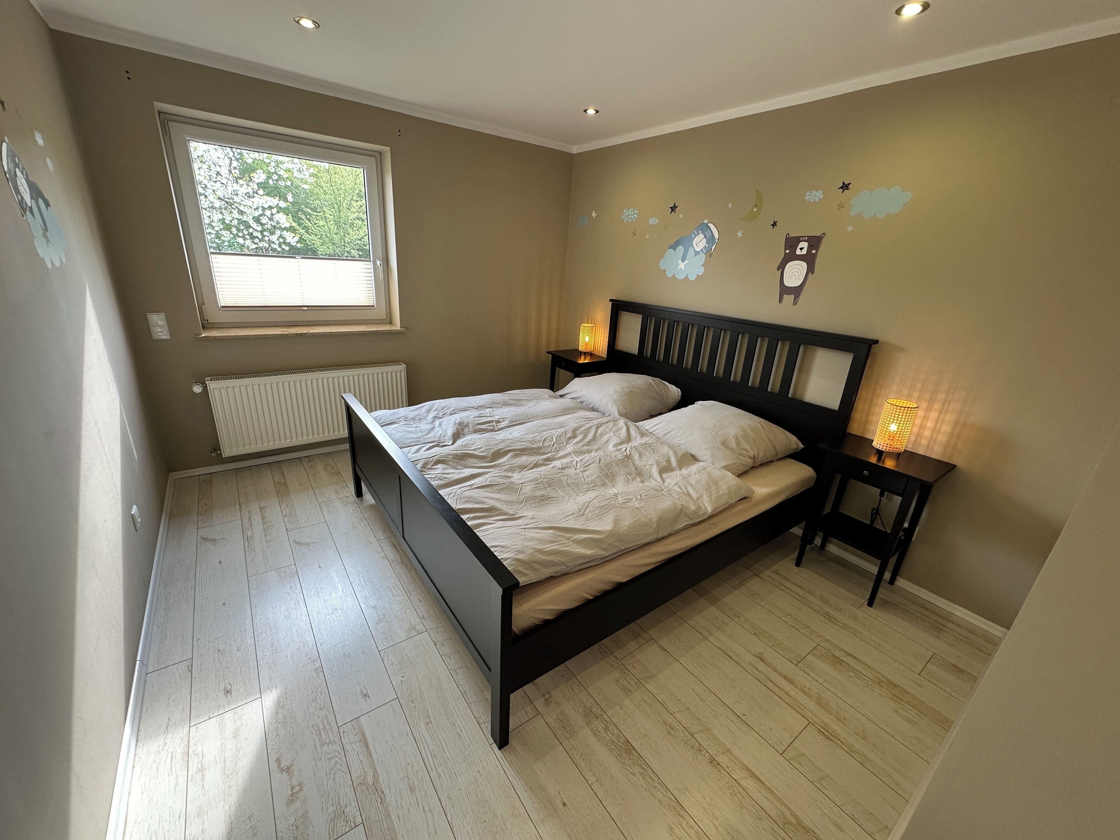 Un dormitorio con cama, ventana, radiador y adornos en la pared.