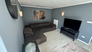 Moderni olohuone, jossa on kulmasohva, litteänäyttöinen televisio, veistos ja seinällä oleva taulu.