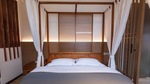 Una cama con cabecera de madera, ropa de cama blanca y dosel.