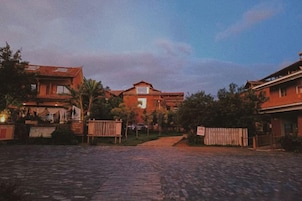 Uma rua de paralelepípedos com edifícios de ambos os lados, uma cerca de madeira e céu claro.