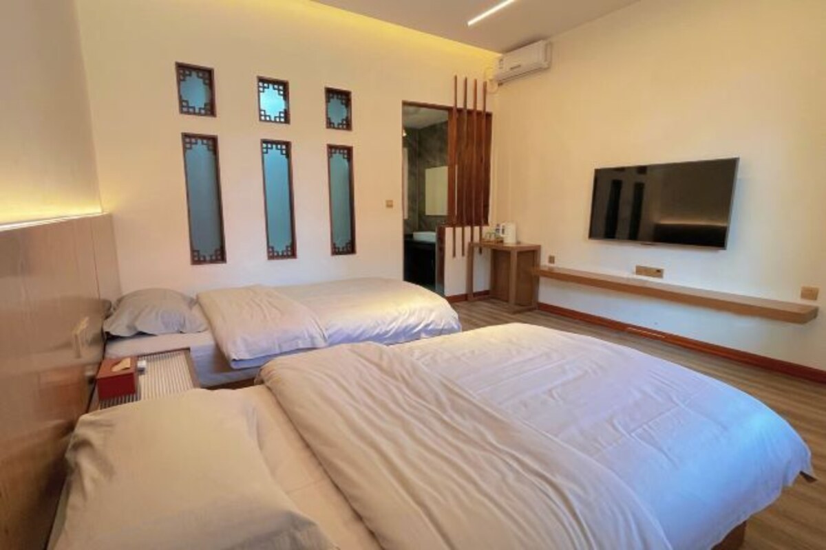 Habitación de hotel con dos camas, un televisor montado en la pared y suelo de madera.