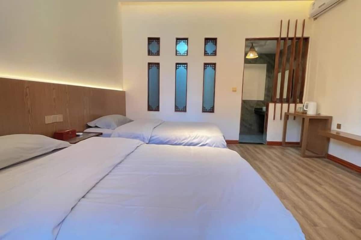 Quarto de hotel com duas camas, cabeceira de madeira, uma mesa pequena com chaleira e um painel decorativo fixado na parede.