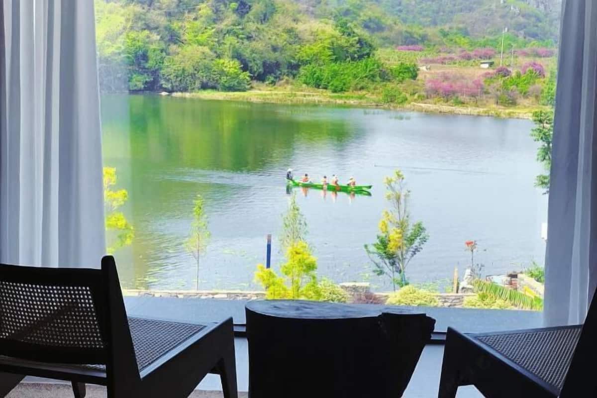 Vista de um lago com um barco a remo, pessoas, uma cadeira e uma mesa em primeiro plano.