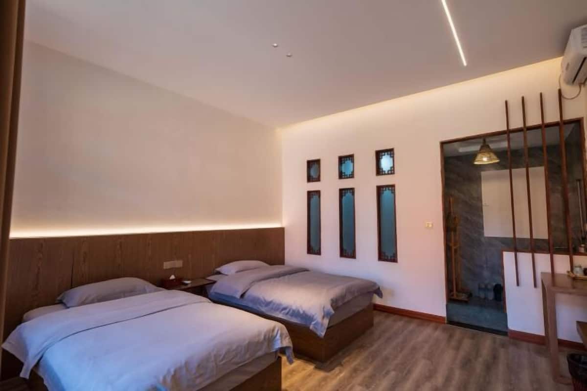Quarto de hotel moderno com duas camas, cabeceira de madeira, uma pequena escrivaninha e um espelho.
