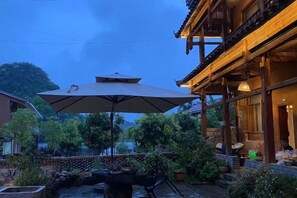 An outdoor seating area with a table and chairs, a large umbrella, and a decorative fountain. - Leisure Courtyard Lake View Homestay (Qiubei)