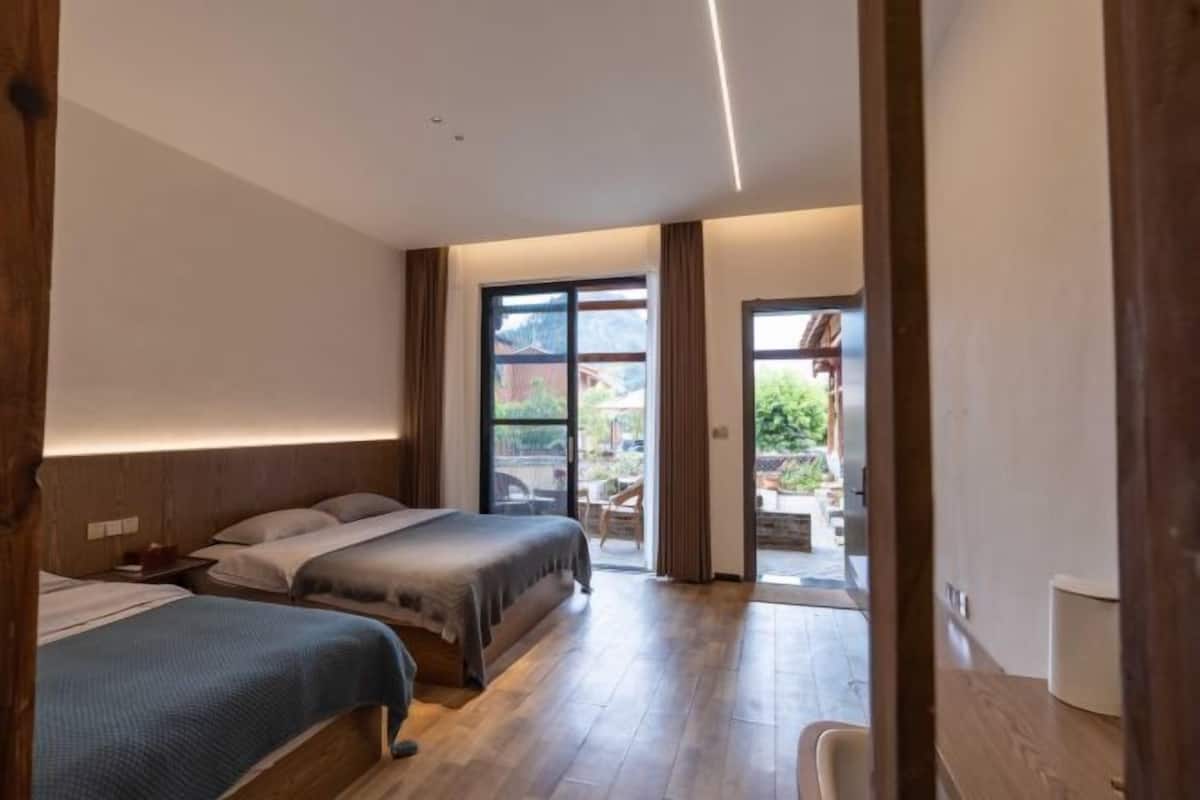 Quarto de hotel com duas camas, piso de madeira e vista para o exterior por uma porta de vidro deslizante.