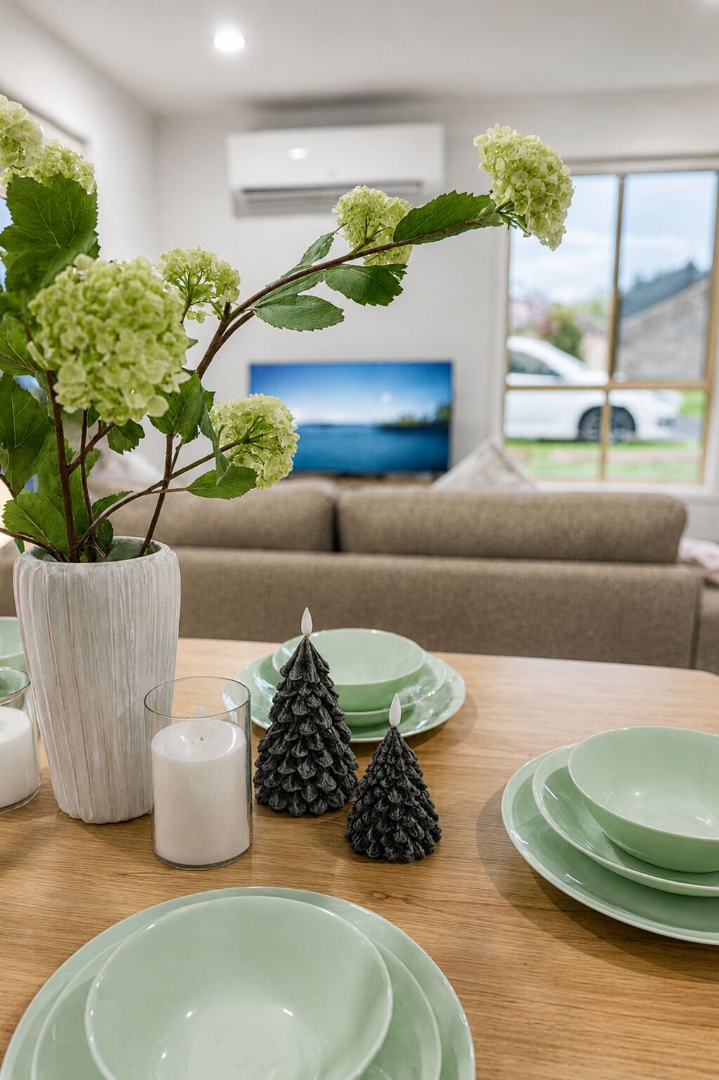 A dining table with green plates, a white vase with green flowers, and two pinecone decorations.