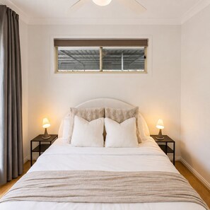 A bedroom with a bed, two bedside tables, a window, and a ceiling fan.