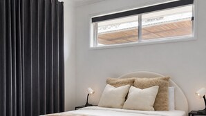 Ein Schlafzimmer mit einem Bett, zwei Nachttischen, einem Fenster und einem Vorhang.