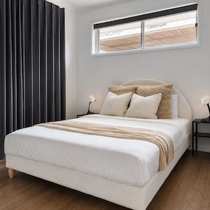 A bedroom with a bed, two bedside tables, a window, and a curtain. - Relax & Unwind in Sunnybank Spacious 3BR Home w Parking (Sunnybank Hills)