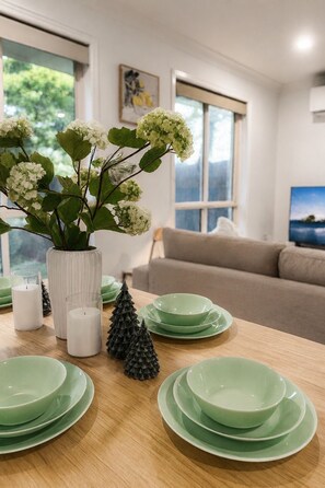 A dining area with a wooden table set with green plates and a vase with white flowers. - Relax & Unwind in Sunnybank Spacious 3BR Home w Parking (Sunnybank Hills)