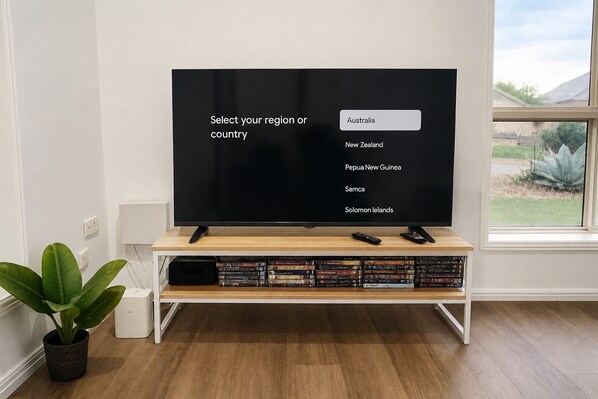 A television on a wooden stand with a remote control, a selection menu on the screen, and a plant beside it.