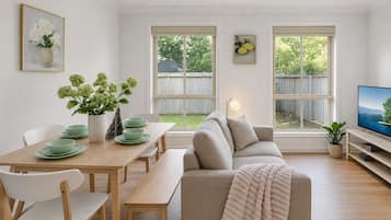 A modern living room with a sofa, dining table, chairs, and a television.