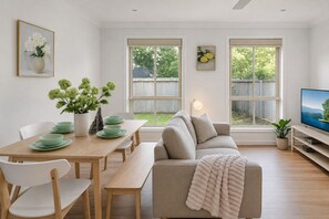 A modern living room with a sofa, dining table, chairs, and a television. - Relax & Unwind in Sunnybank Spacious 3BR Home w Parking (Sunnybank Hills)