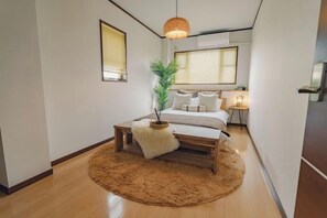 A bedroom with a bed, bedside table, lamp, and a large window with blinds. - JS xiaozhai・yuishima (Osaka)