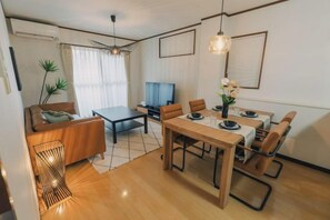 A modern living room with a sofa, coffee table, dining table, and chairs. There is a television and a plant in the room. - JS xiaozhai・yuishima (Osaka)