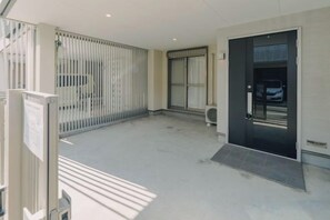 A clean, modern entrance with a glass door, a metal gate, and a small step leading to a parking area. - JS xiaozhai・yuishima (Osaka)