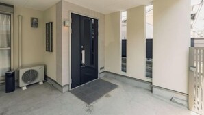 A clean, modern entrance with a black door, a small air conditioning unit, and a tiled entrance mat. - JS xiaozhai・yuishima (Osaka)