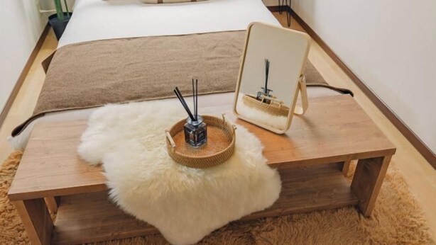 A neatly arranged bedroom with a bed, a wooden bedside table, a fluffy white rug, and a small wooden stool. - JS xiaozhai・yuishima (Osaka)