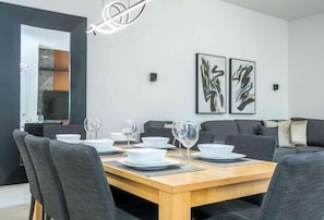A modern dining area with a wooden table set for four, grey upholstered chairs, and abstract wall art. - Cozy, Perfect for Families, Hot Tub & Grill - 3013 (Kissimmee)