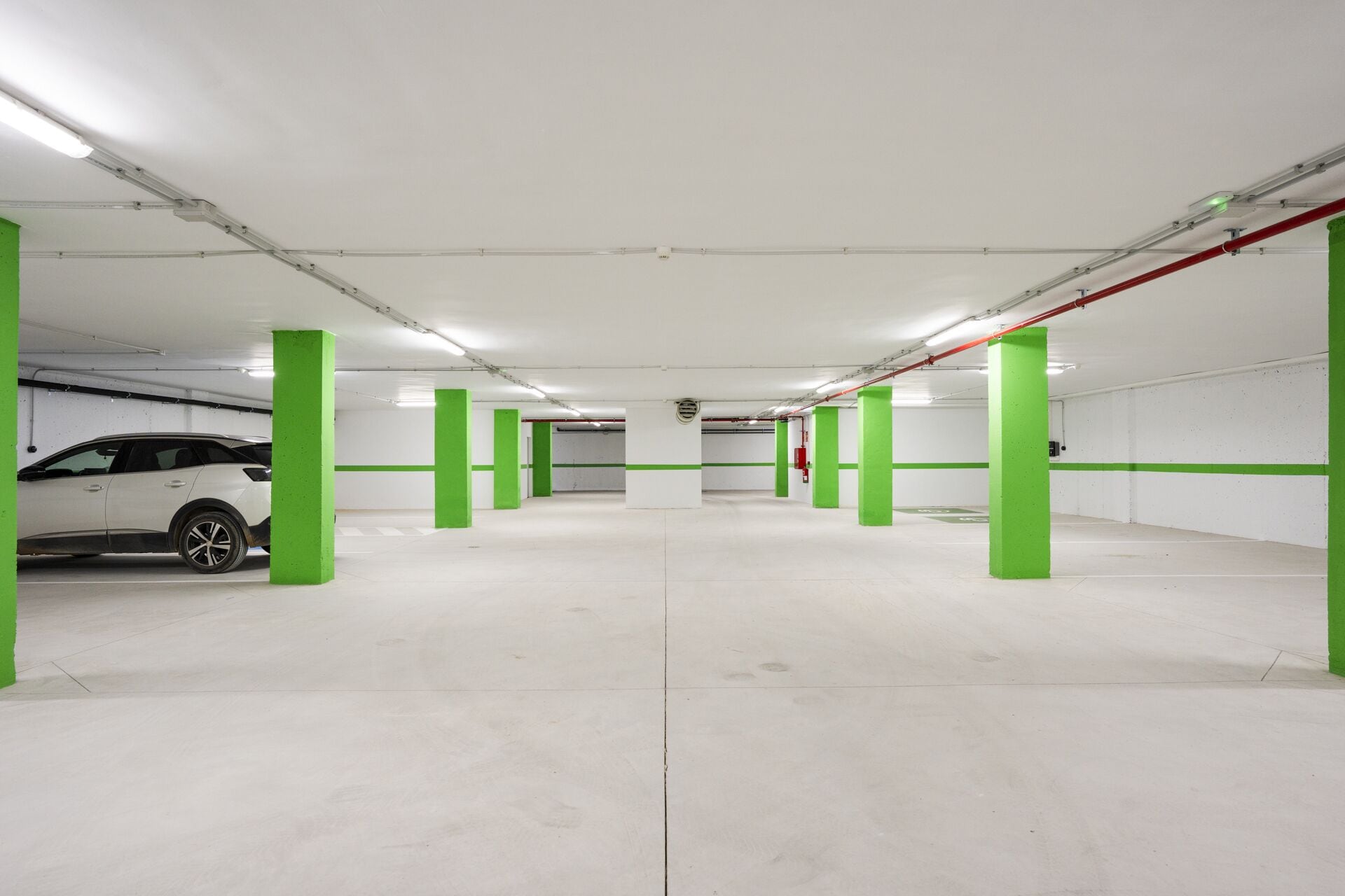 A parking garage with white walls, green pillars, and a white car parked in the foreground.