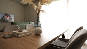 A modern hotel room with a wooden dining table, a vase with pampas grass, a bowl, and a book. There is a green sofa in the background and a painting on the wall. - Alora Apartamentos Mérida (Mérida)