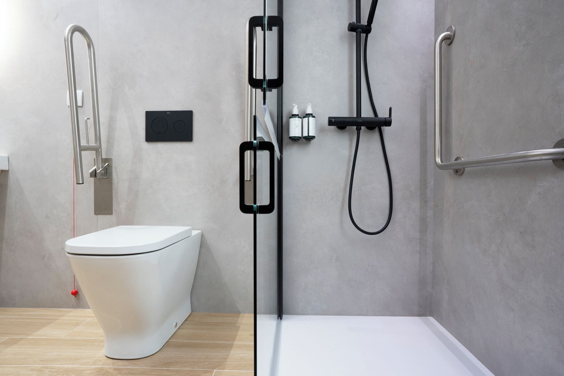 A modern bathroom with a white toilet, a glass shower enclosure, and a handrail.