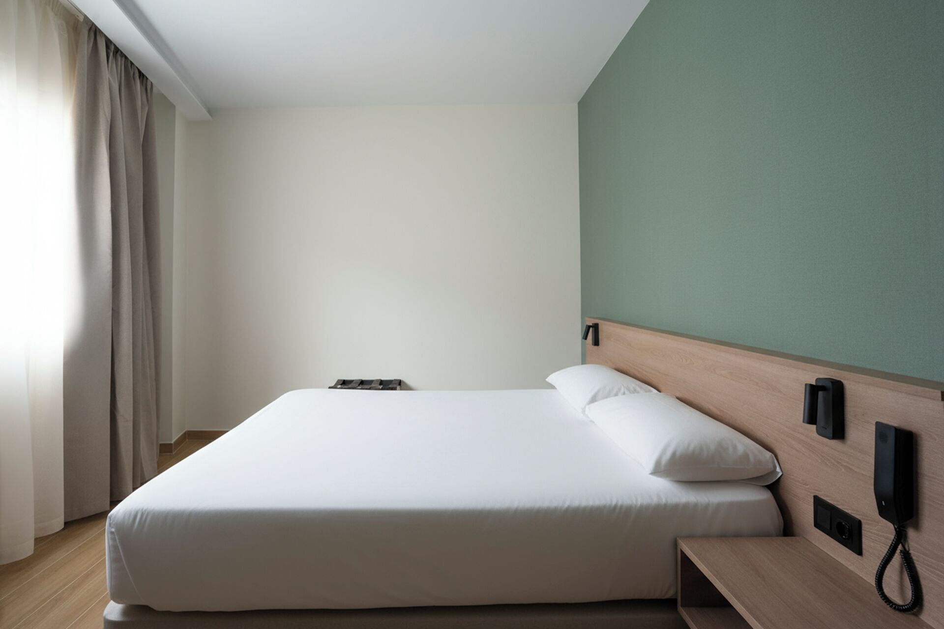 A neatly made bed with a wooden headboard, a bedside table, and a wall-mounted phone.