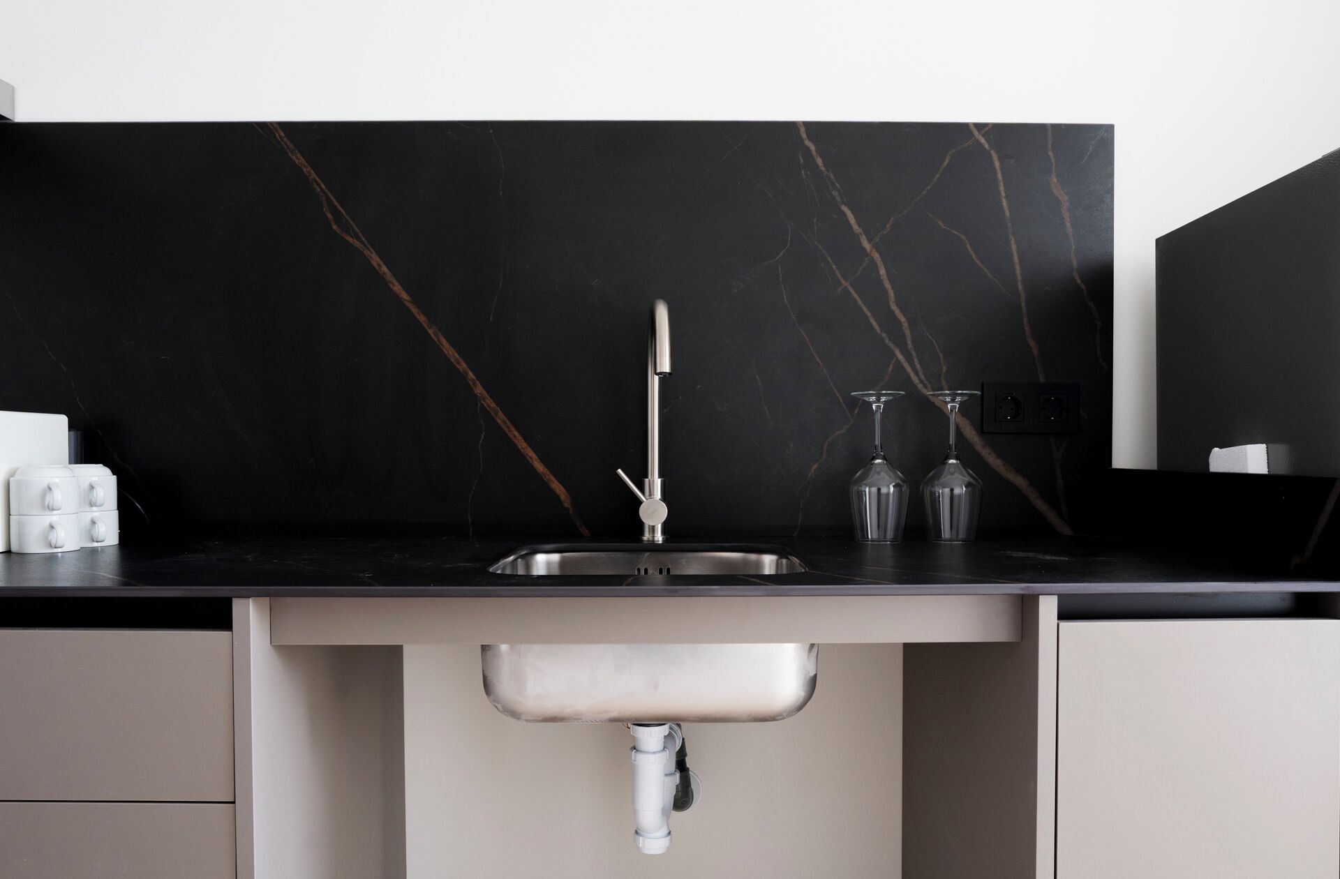 A modern kitchen with a black marble backsplash, stainless steel sink, and a white cabinet below.