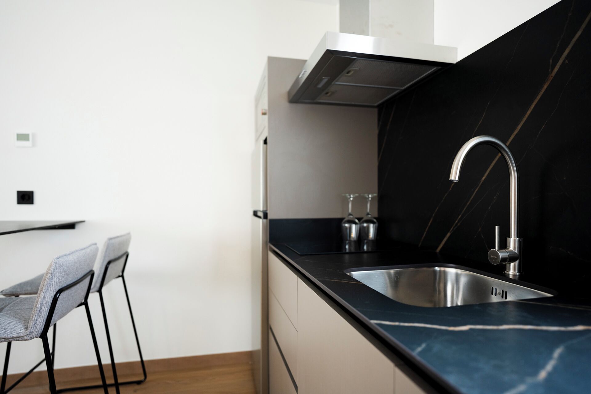 Una cuina moderna amb taulell de marbre negre, vàter d'acer inoxidable i aixeta moderna. Hi ha dos tamborets d'esbarjo i una petita zona de bar.
